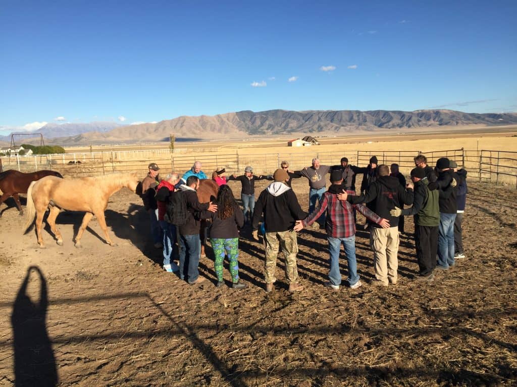 A group of people in a circle with horses nearby